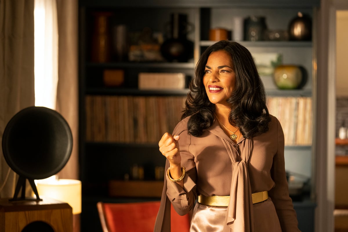 Sarita Choudhury as Seema Patel smiling, holding a purse