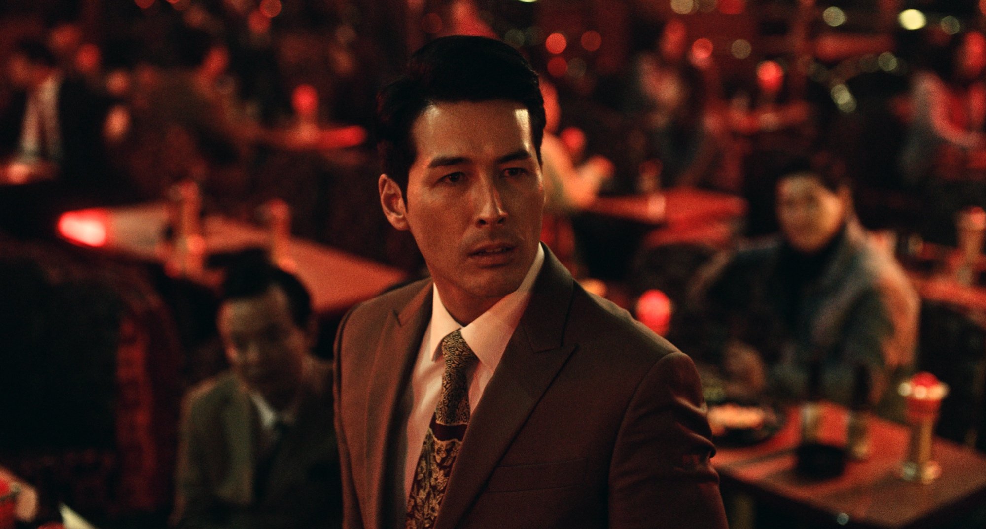 Sean Dulake as Joon Park in 'Dramaworld' Season 2 wearing a suit and tie.
