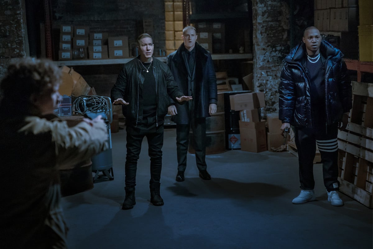 Joseph Sikora as Tommy Egan, Shane Harper as Vic Flynn, and Kris D. Lofton as Jenard standing in a dark warehouse with guns pointed at them in 'Power Book IV: Force'