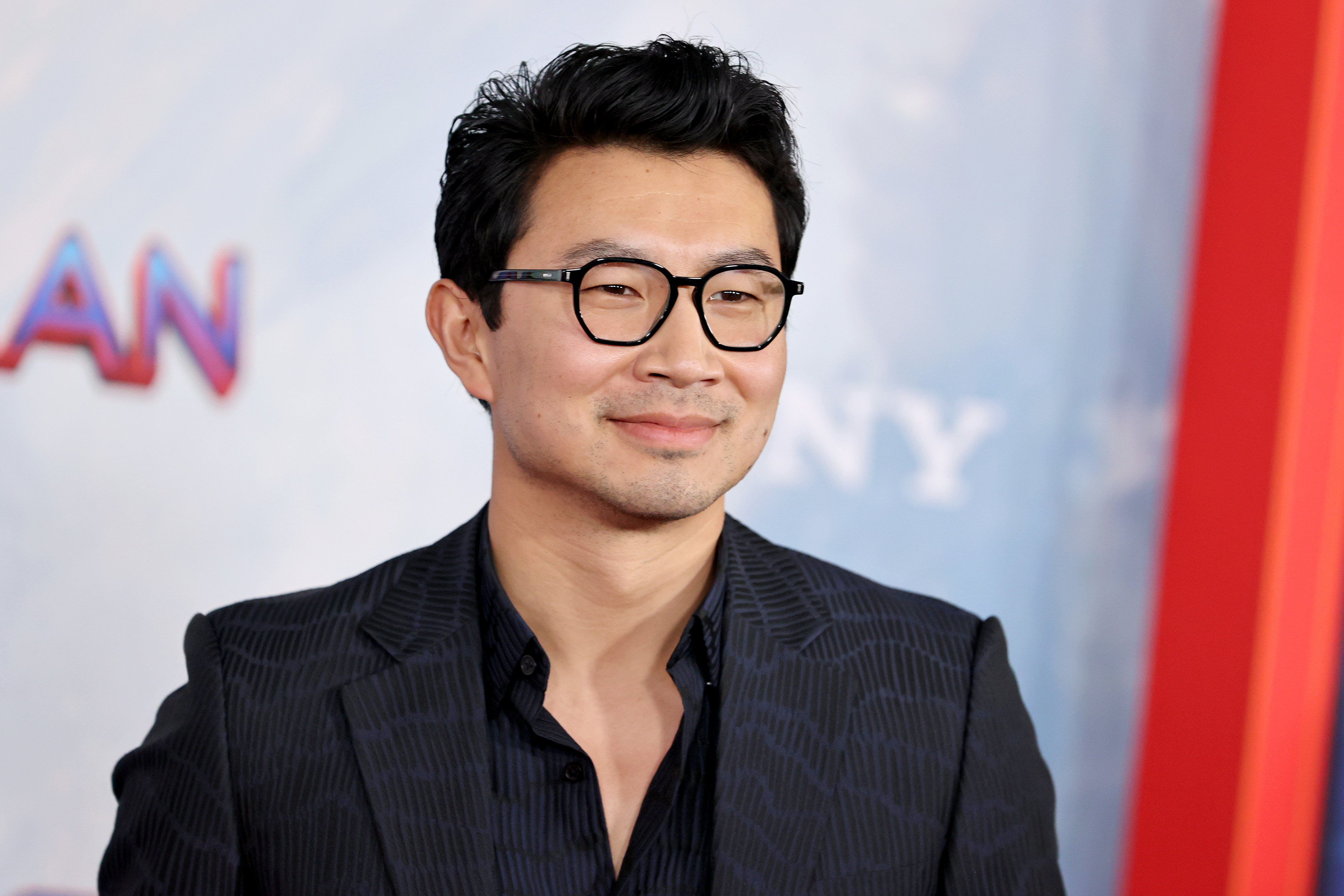 'Shang-Chi and the Legend of the Ten Rings' star Simu Liu wears a patterned black suit over a black button-up shirt and black-framed glasses.