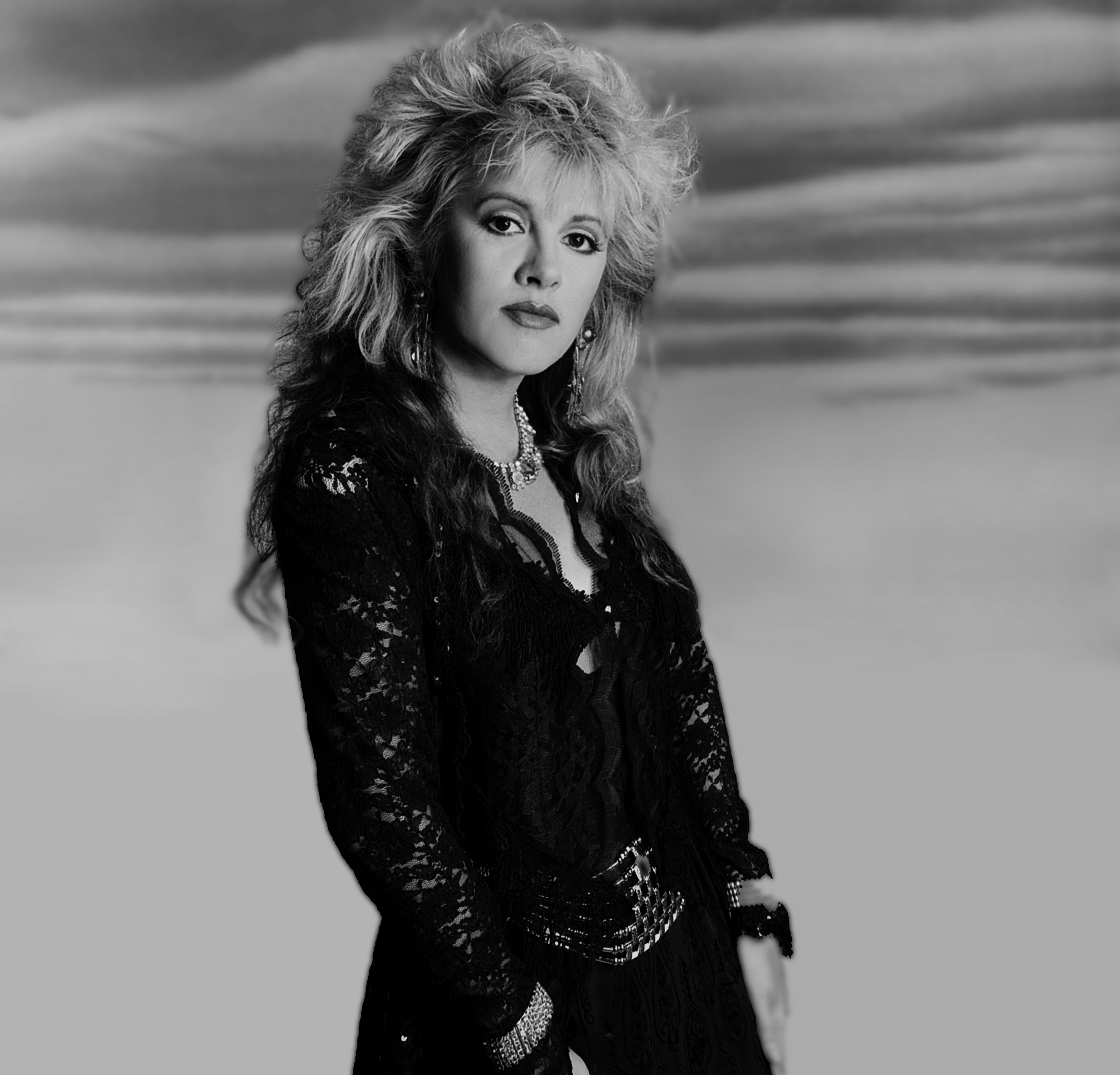 A black and white photo of Stevie Nicks in a black lace shirt. She was in Fleetwood Mac with her ex Lindsey Buckingham.