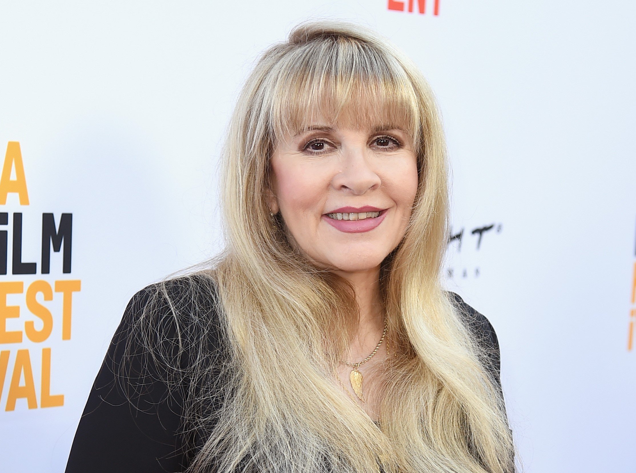 Stevie Nicks wears a black shirt and stands in front of a white background.