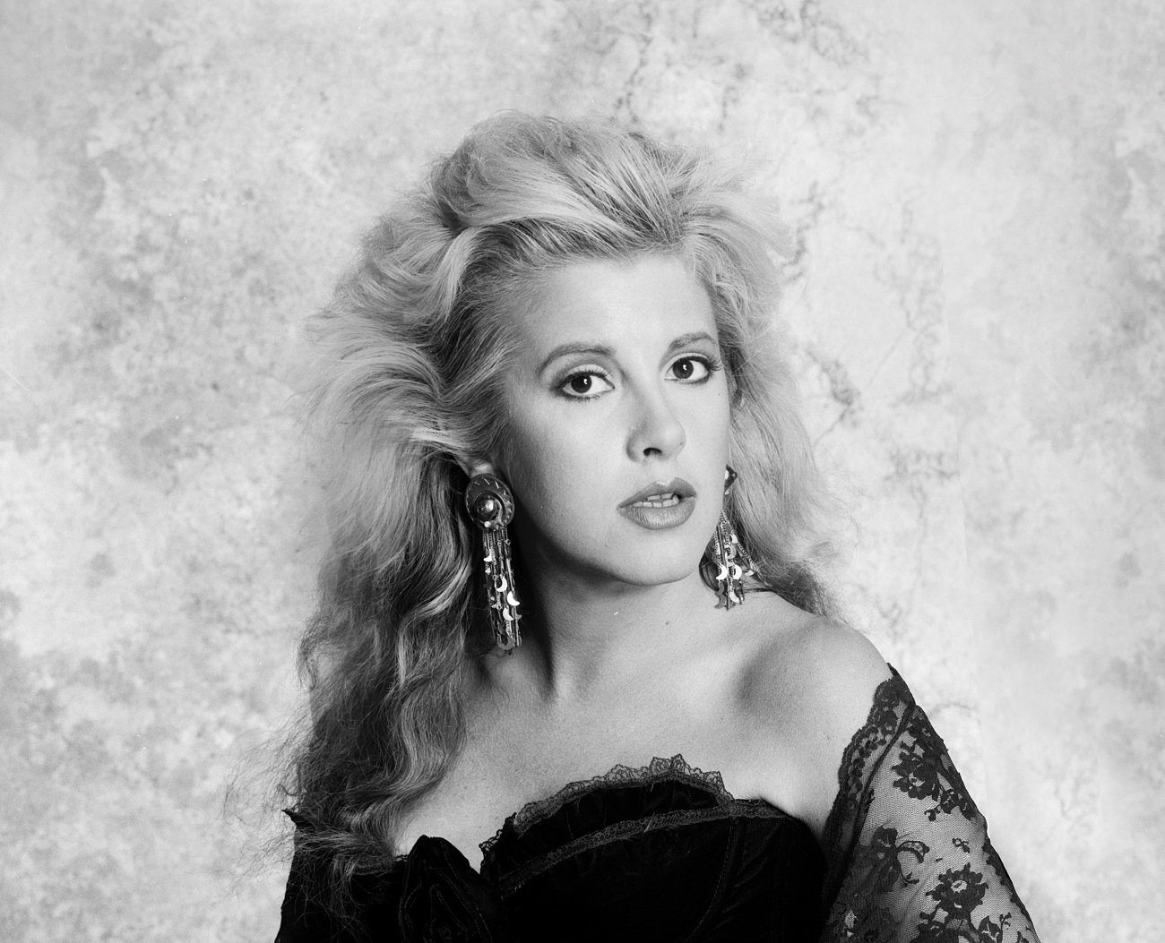 A black and white photo of Stevie Nicks wearing a black lace dress against a gray background.