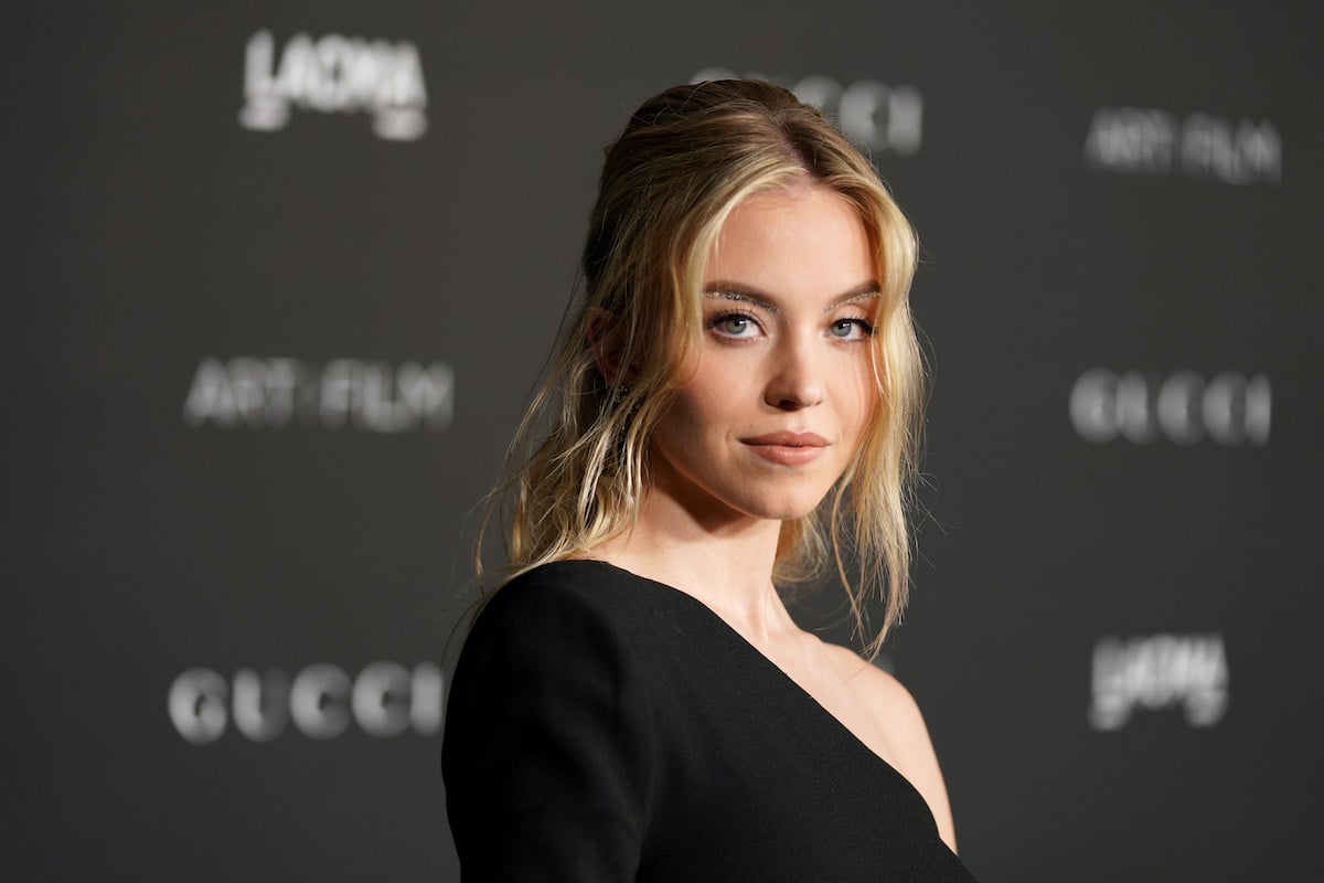 Sydney Sweeney smirks at the camera in a black dress