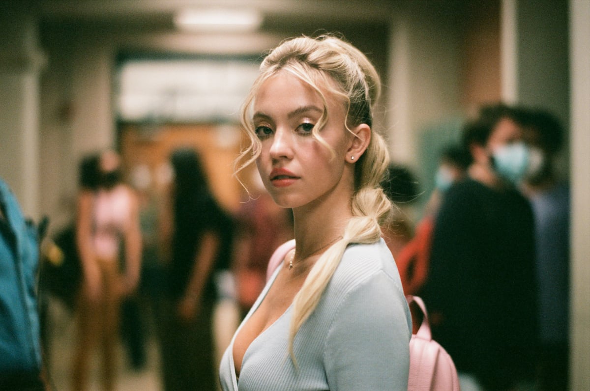 Sydney Sweeney in character as Cassie in Euphoria Season 2. Cassie wears a low-cut blue top and her hair is in a ponytail.