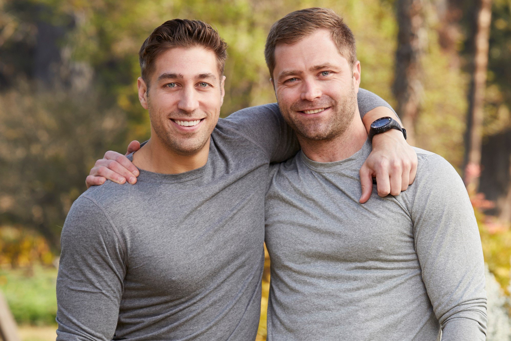 'The Amazing Race' Season 33 contestants Ryan Ferguson and Dusty Harris wear gray long-sleeved shirts and wrap their arms around one another while posing for promotional pictures.