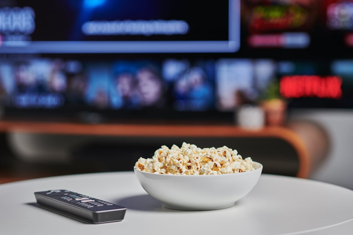 A bowl of popcorn and TV remote control on a coffee table, with Netflix streaming on a television in the background