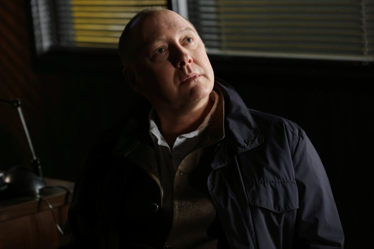 James Spader as Raymond Reddington in The Blacklist Season 9. Red looks up at someone. He is wearing a dark blue jacket and white collared shirt.