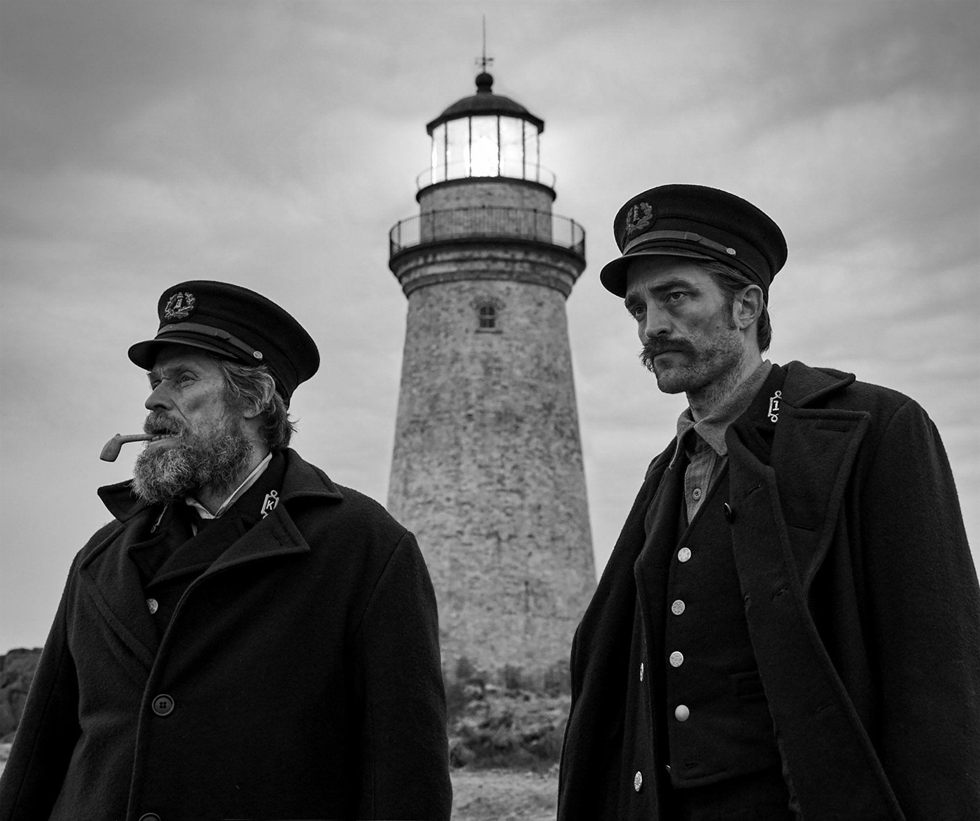 'The Lighthouse' Willem Dafoe as Thomas Wake and Robert Pattinson as Thomas Howard standing in front of a lighthouse