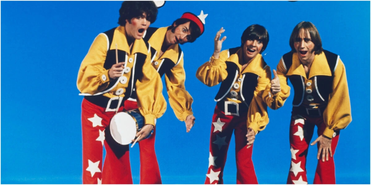 The Monkees pose wearing red pants, yellow shirts and black vests.