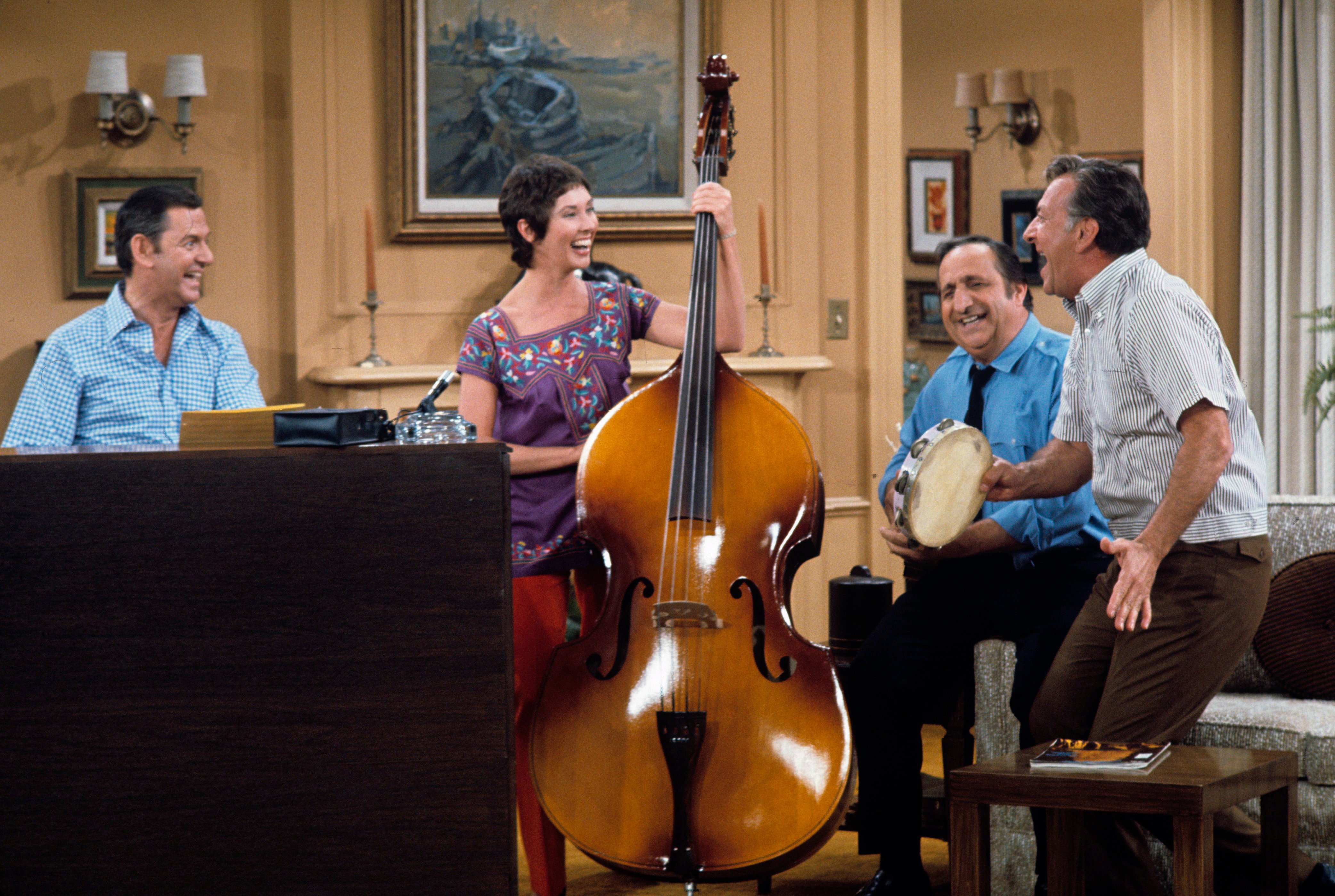 Actor Elinor Donahue plays a stand-up bass in a scene from the 1970s sitcom 'The Odd Couple.' Left to right as well are actors Tony Randall, Al Molinaro, and Jack Klugman.