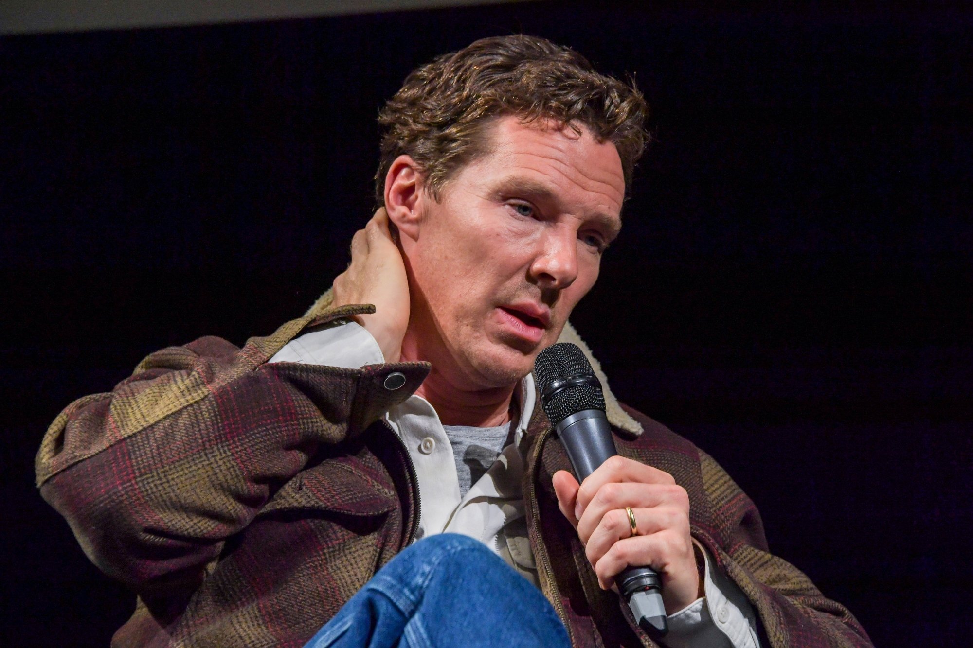 'The Power of the Dog' Phil Burbank actor Benedict Cumberbatch with his hand on his neck and talking into the microphone