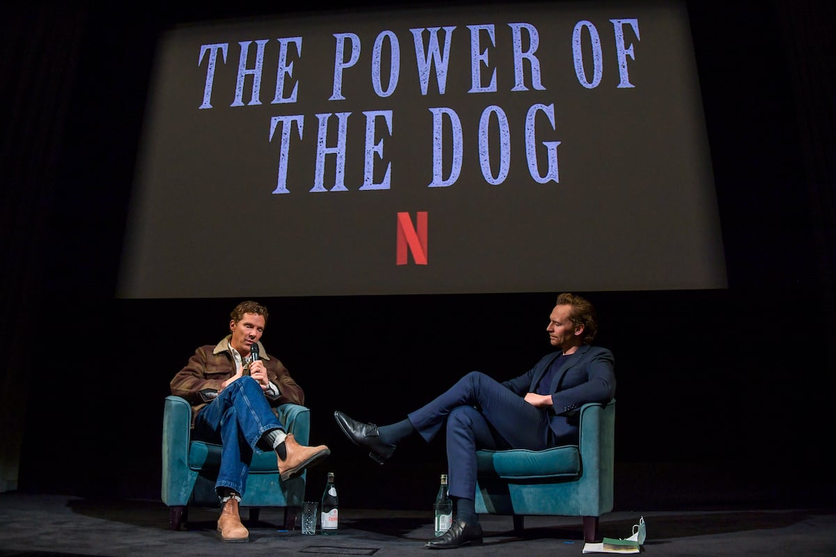 Benedict Cumberbatch and Tom Hiddleston sit in armchairs onstage under ‘The Power of the Dog' logo