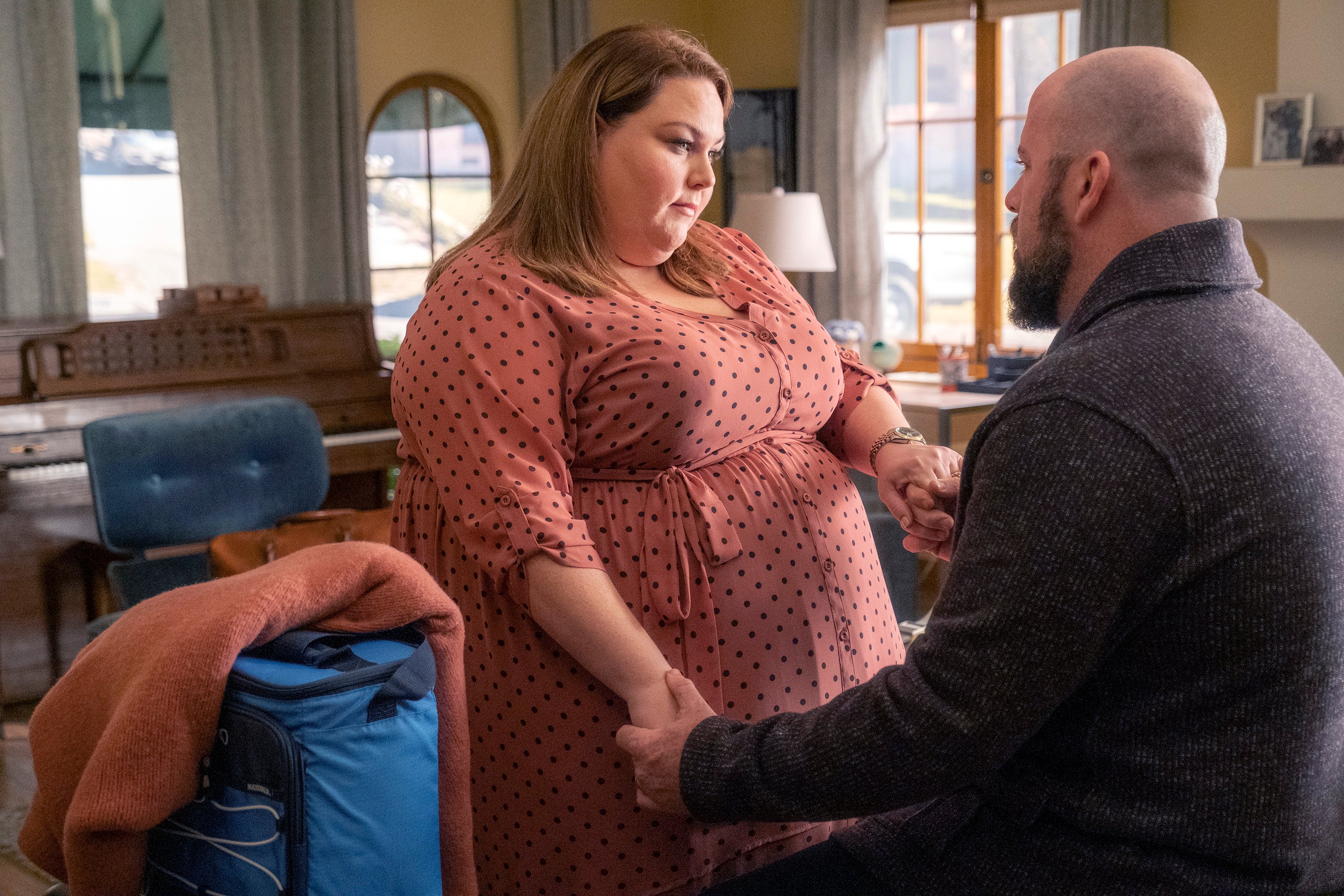 'This Is Us' Season 6 stars Chrissy Metz and Chris Sullivan, in character as Kate and Toby, share a scene. Toby, holding Kate's hands, wears a dark gray sweater. Kate wears a pink dress with black polka dots.