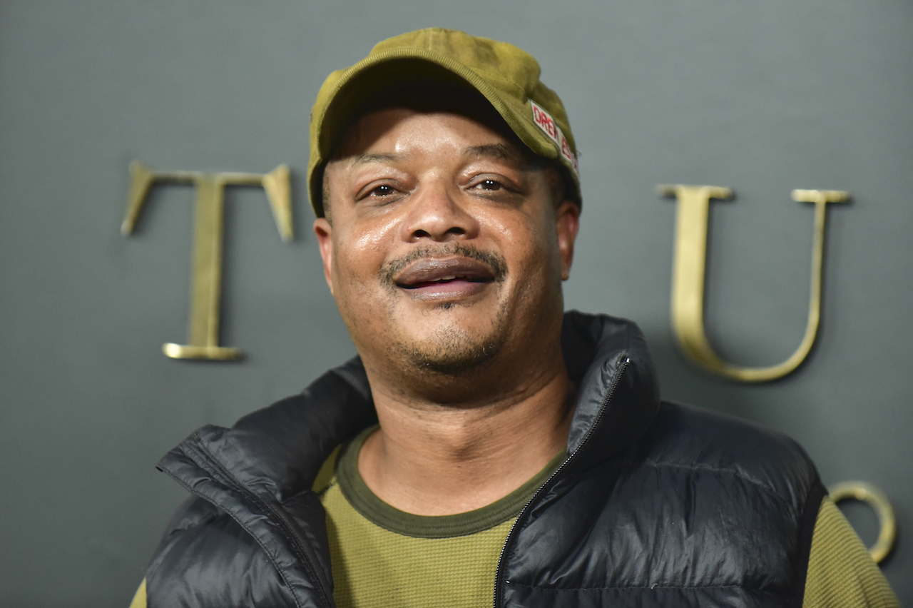 Todd Bridges attends the Premiere of Apple TV+'s "Truth Be Told" wears a green shirt, black jacket, and a green hat.