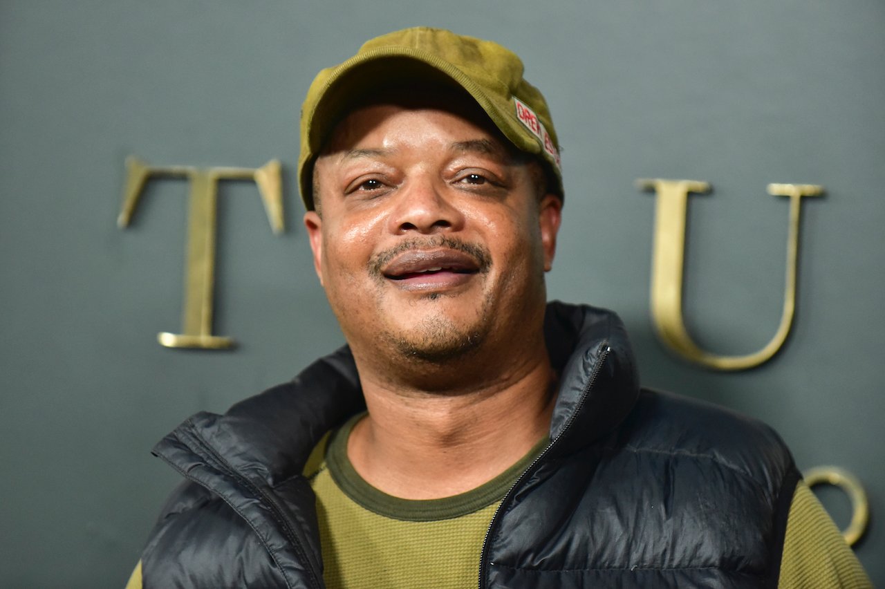 Todd Bridges attends the Premiere of Apple TV+'s "Truth Be Told" wears a green shirt, black jacket, and a green hat.