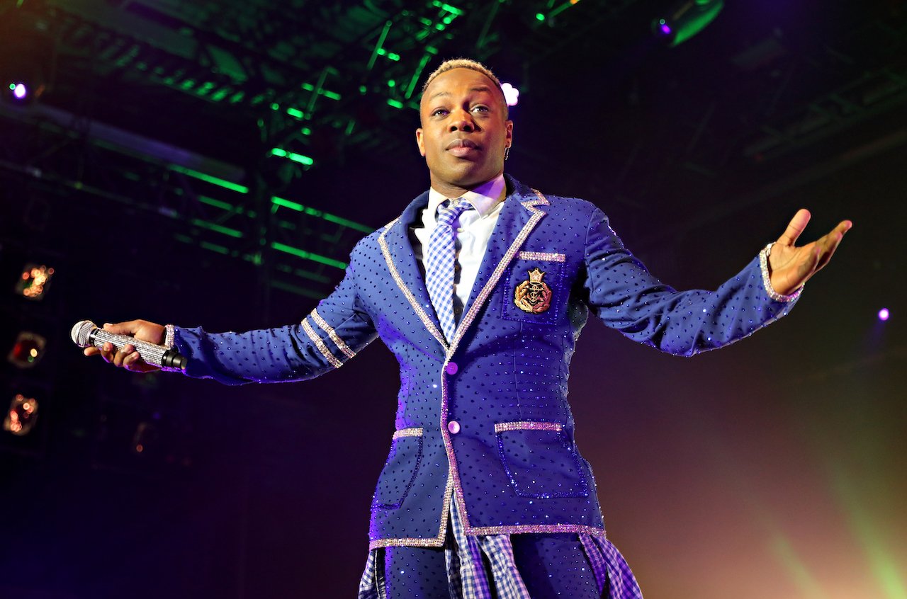 Todrick Hall stands on stage with his arms open wearing a purple outfit.