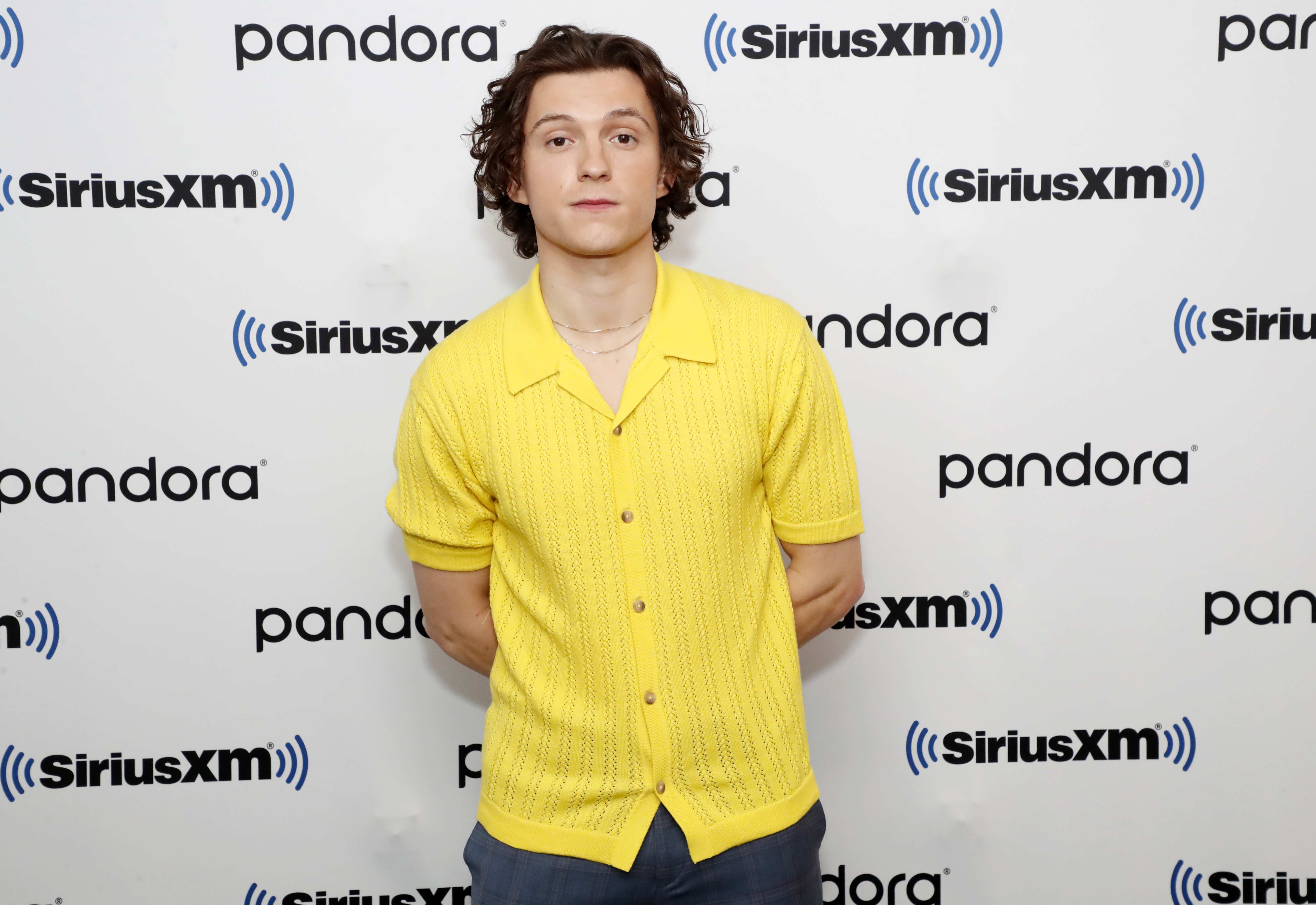 'Spider-Man: No Way Home' star Tom Holland wears a yellow button-up short-sleeved shirt over dark gray pants.