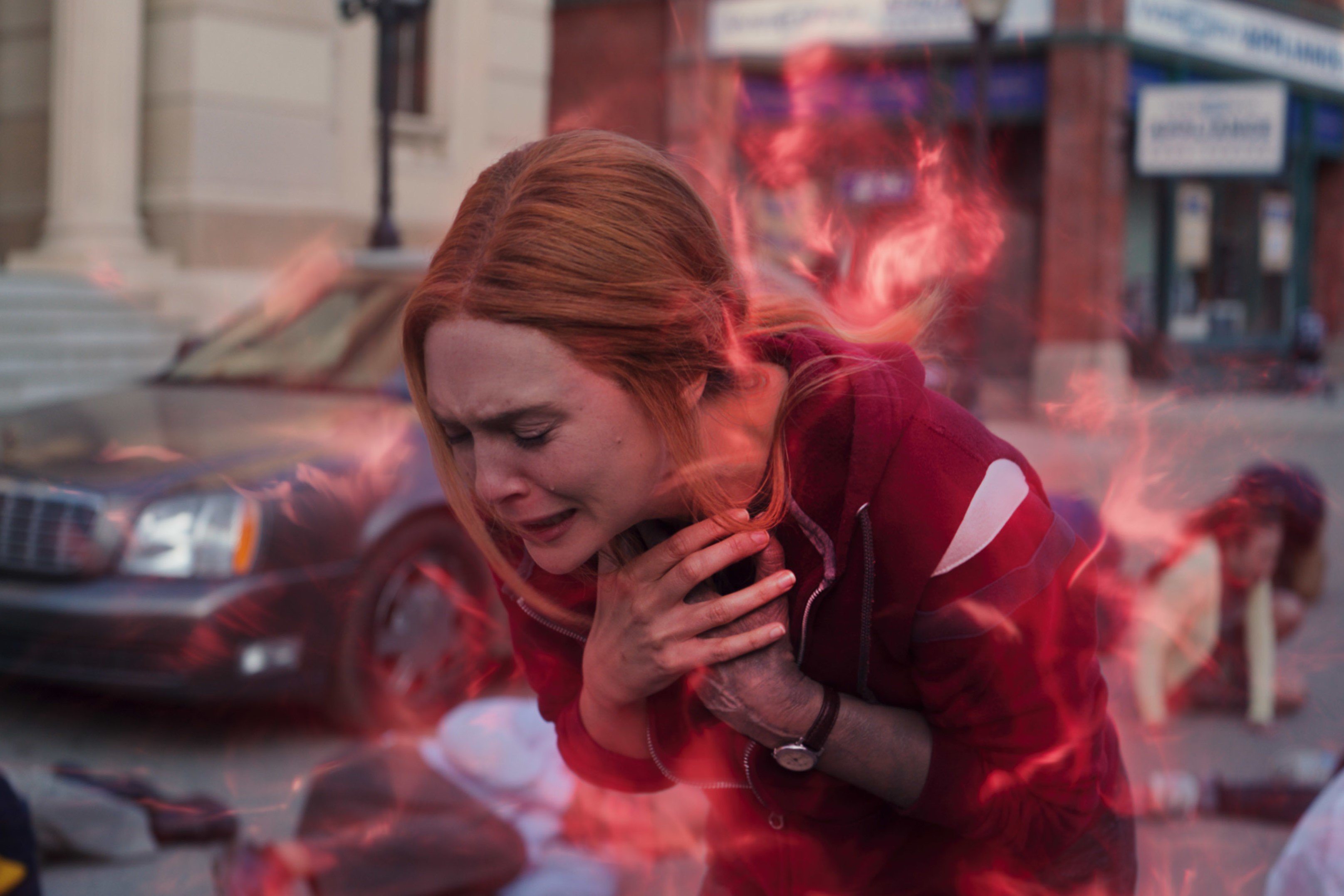 'Doctor Strange 2' star Elizabeth Olsen, in character as Scarlet Witch, wears a red hoodie. She is surrounded by red magic in the photo as she bends over and clutches her chest.