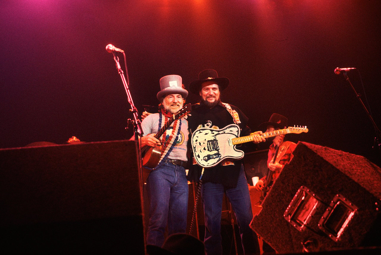 Willie Nelson and Waylon Jennings on stage, both wearing hats and guitars c. 1985