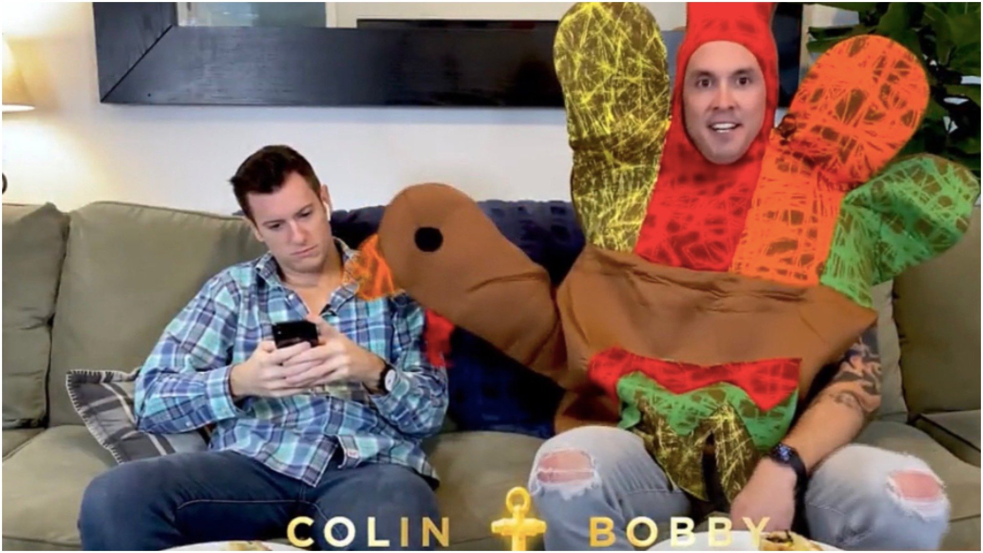 Colin Macy-O'Toole looks at his phone while Bobby Giancola wears a turkey costume while sitting on the couch