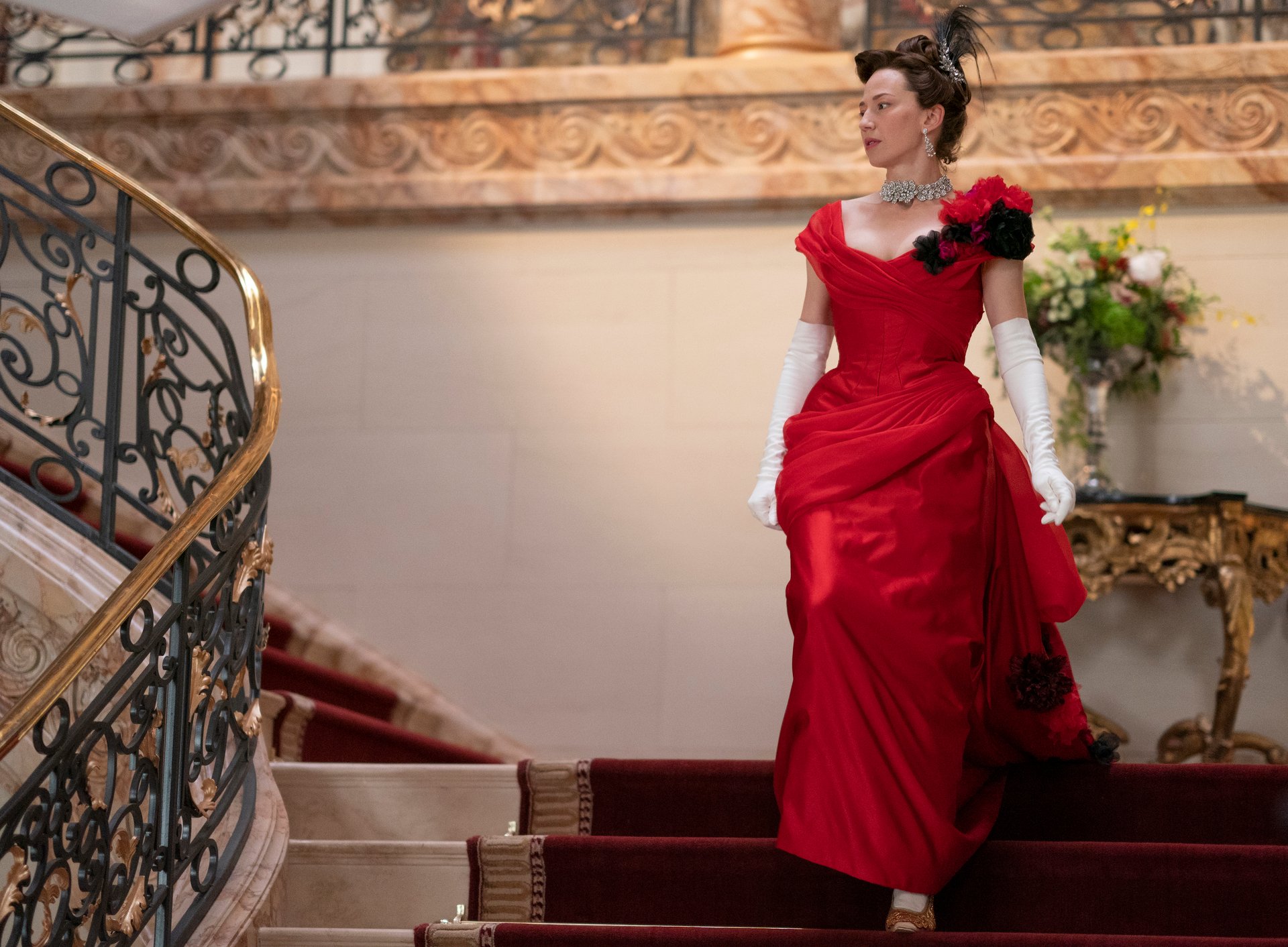 Carrie Coon as Bertha Russell, wearing a red dress and walking down the stairs, in 'The Gilded Aged'
