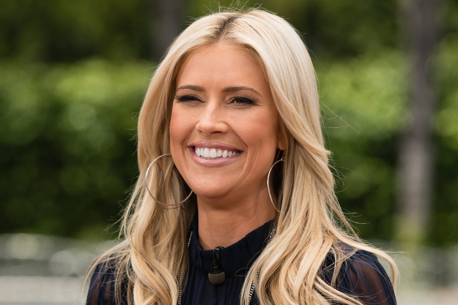 Christina Haack smiling, wearing large hoop earings and a sheer top