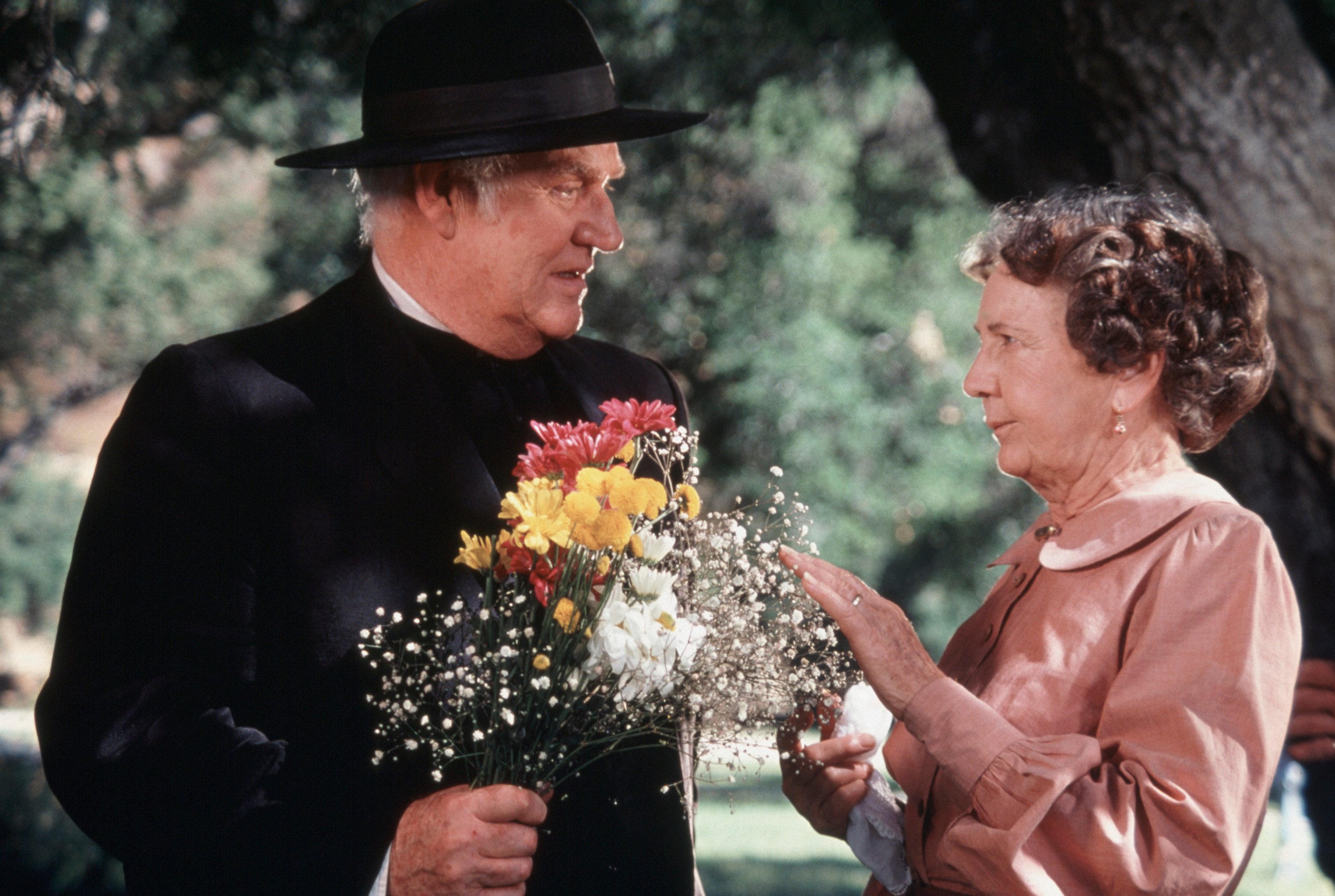 Dabbs Greer holds a bouquet of flowers and talks to a woman during an episode from Little House on the Prairie