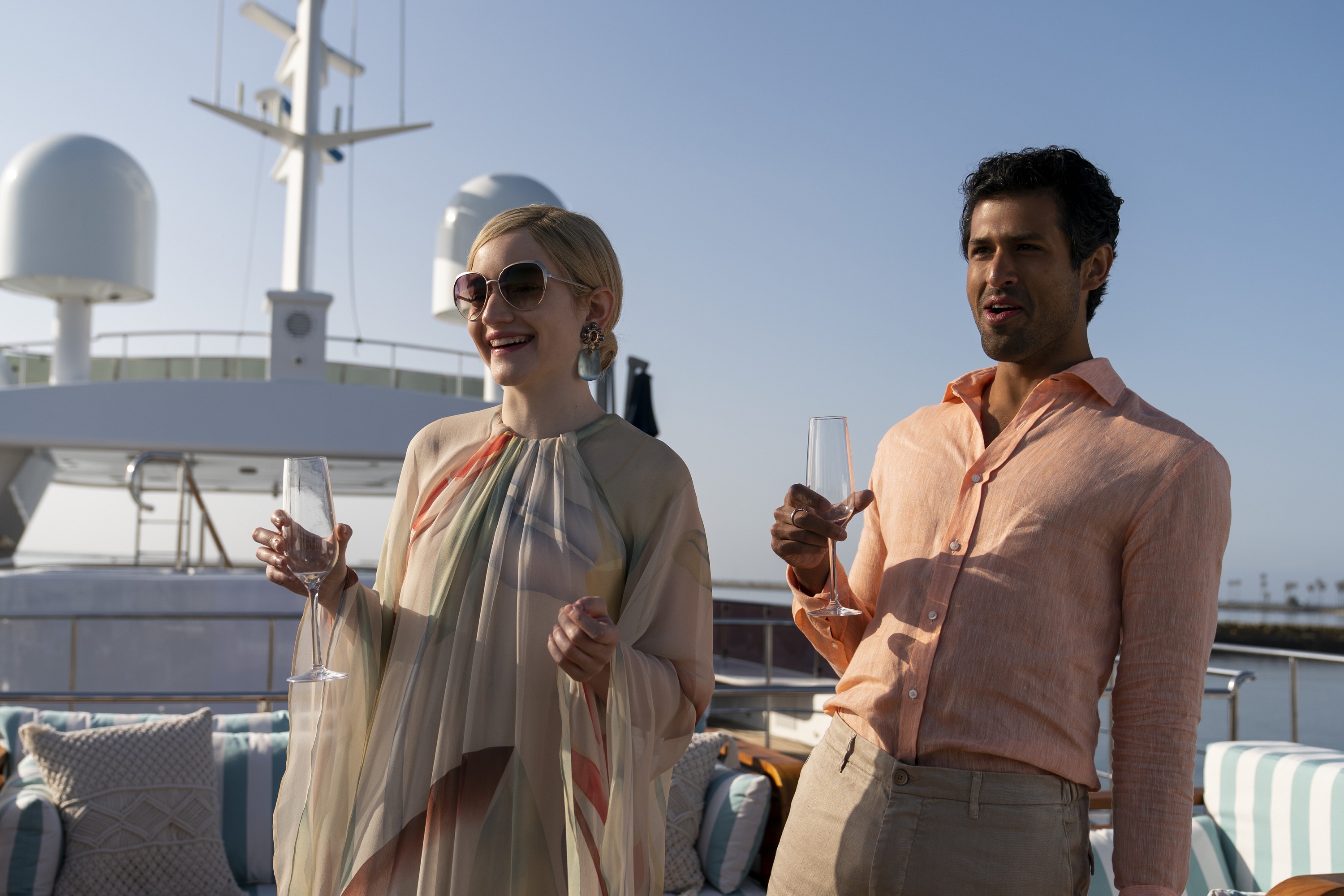 'Inventing Anna' cast members Julia Garner and Saamer Usmani holding drinks on a yacht as Anna Delvey and Chase Sikorski