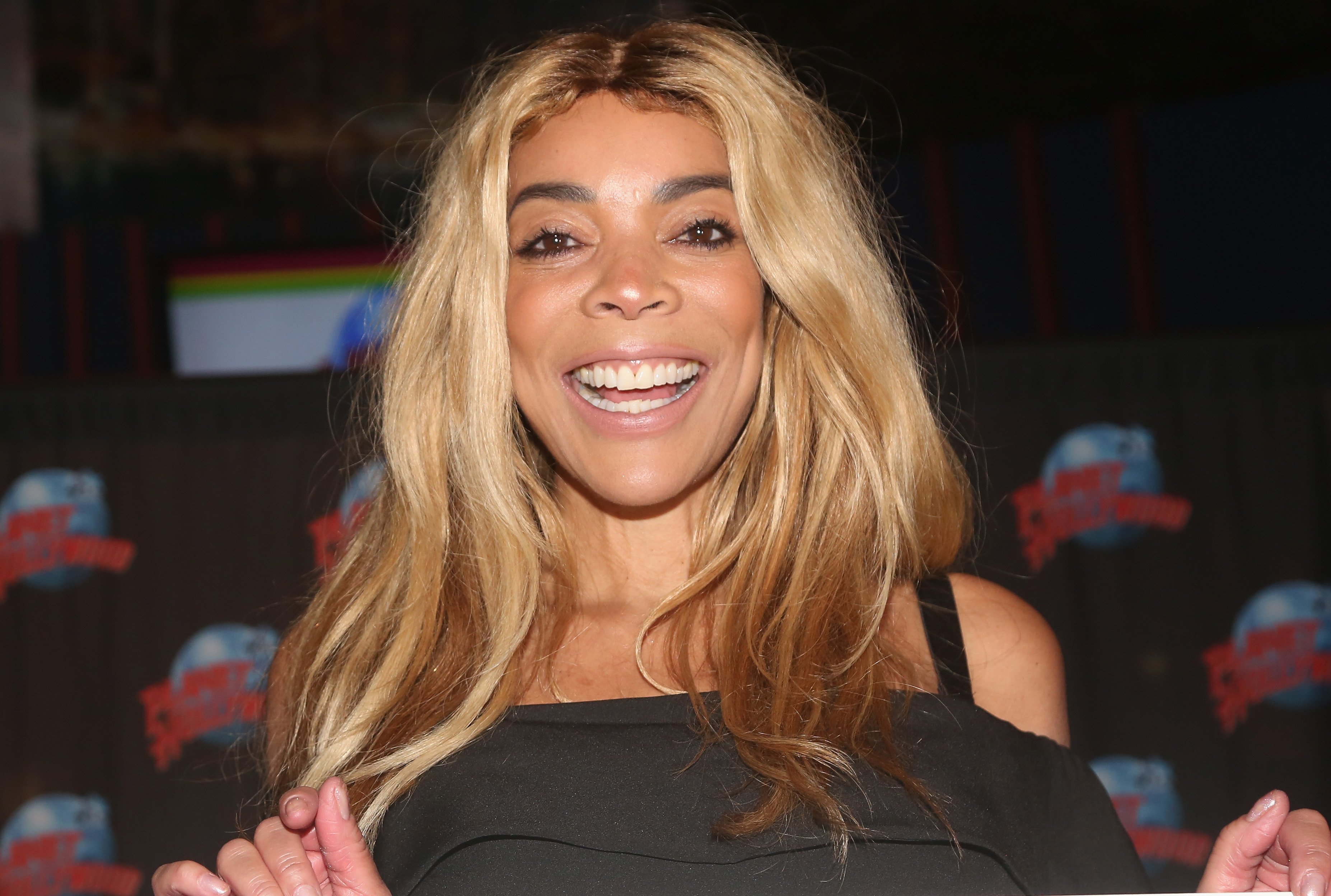 Wendy Williams wearing a black top with her shoulders exposed and smiling for the camera