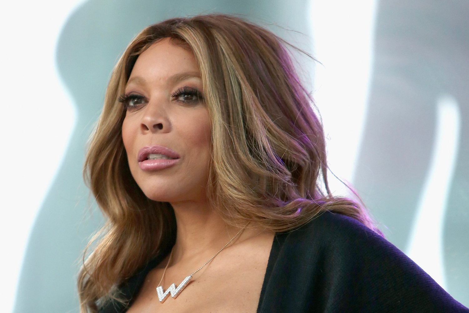 Wendy Williams standing on stage, wearing a necklace with a W