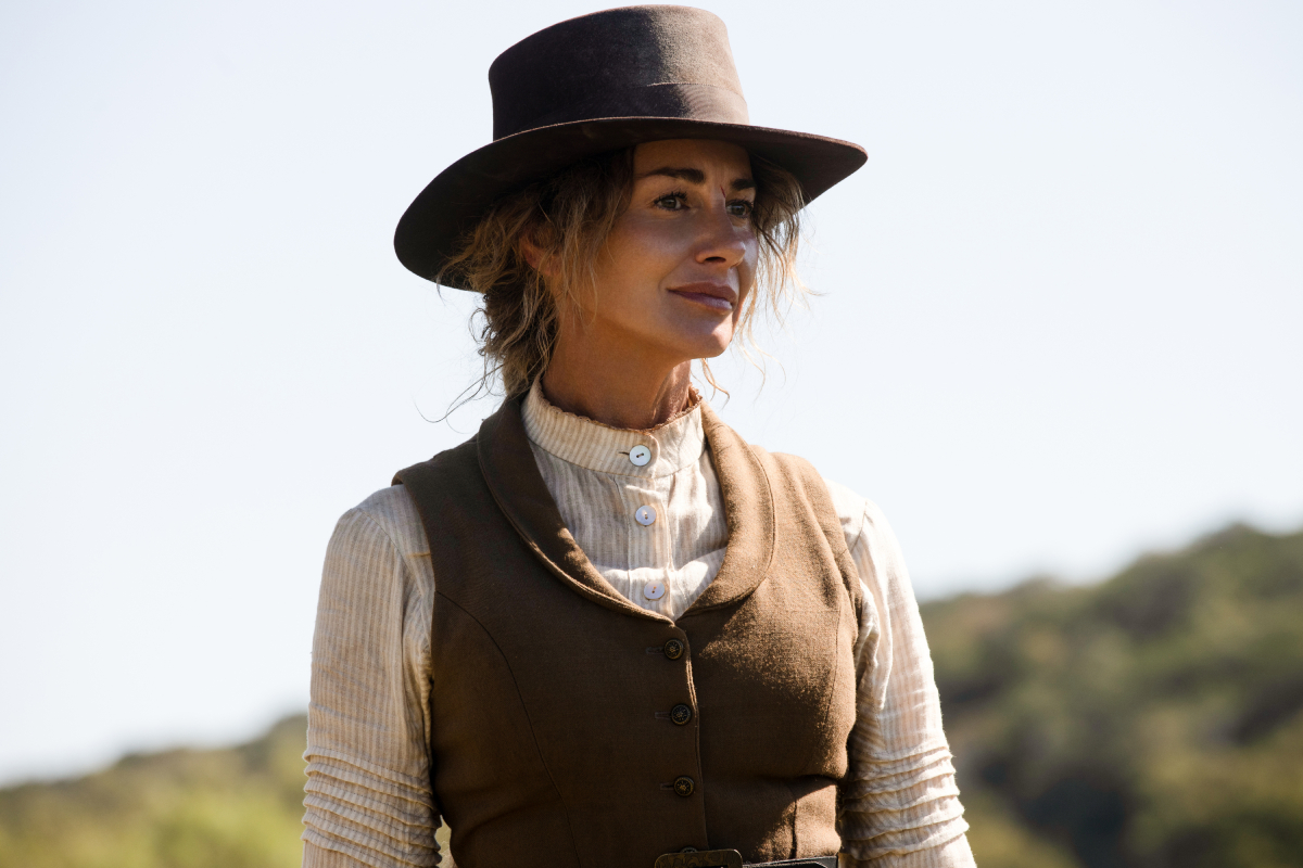 Faith Hill as Margaret in 1883. Margaret wears a brown and white dress and a brown hat.