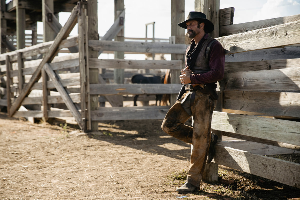 Tim McGraw as James in 1883. James stands against a wooden fence wearing a cowboy hat.