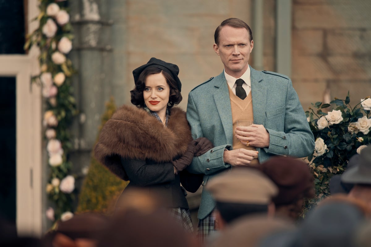 Claire Foy wearing a fur stole standing next to Paul Bettany in blue jacket in 'A Very British Scandal'
