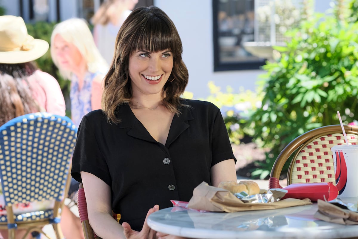 Smiling Abby (Meghan Ory) sitting at a cafe table in 'Chesapeake Shores' Season 5 