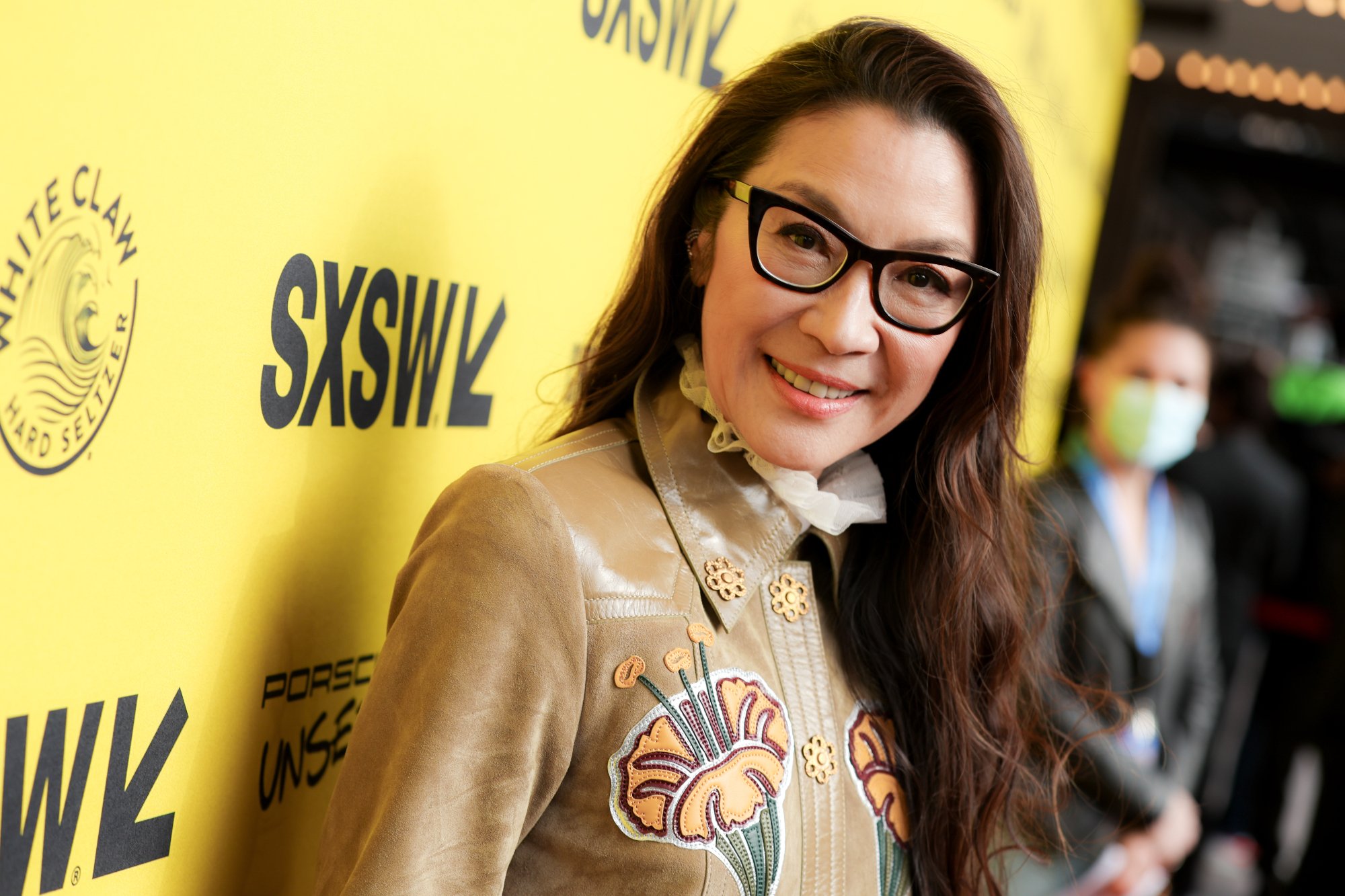 Actor Michelle Yeoh wearing glasses in front of yellow SXSW step and repeat