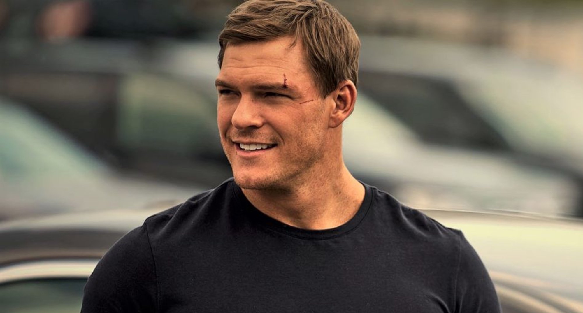 Alan Ritchson as Jack Reacher in 'Reacher' smiling and wearing brown shirt.