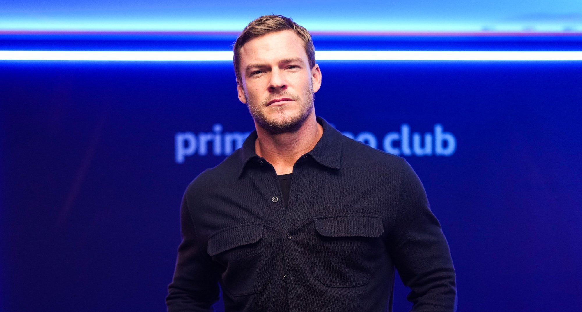 Alan Ritchson from Amazon Prime 'Reacher' series wearing black button-up shirt.