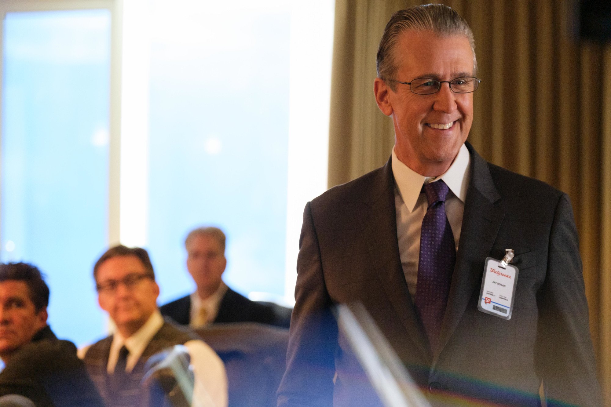 Alan Ruck as Dr. Jay Rosan in 'The Dropout' Episode 4. He's standing in a meeting room and wearing a suit.