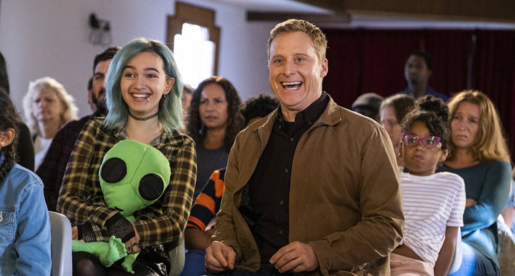 Alan Tudyk and guest star in 'Resident Alien' Season 2 laughing in auditorium and directed by Lea Thompson.