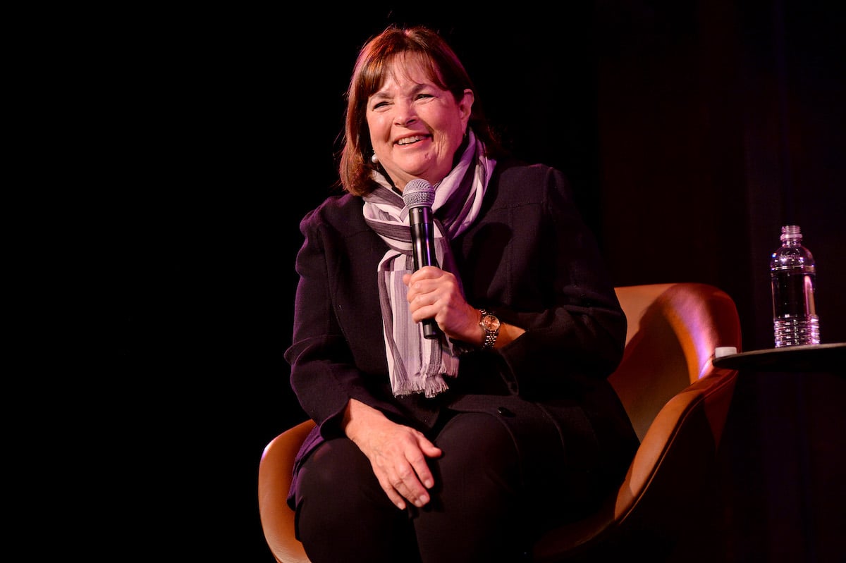 Ina Garten smiles as she sits in a chair holding a microphone