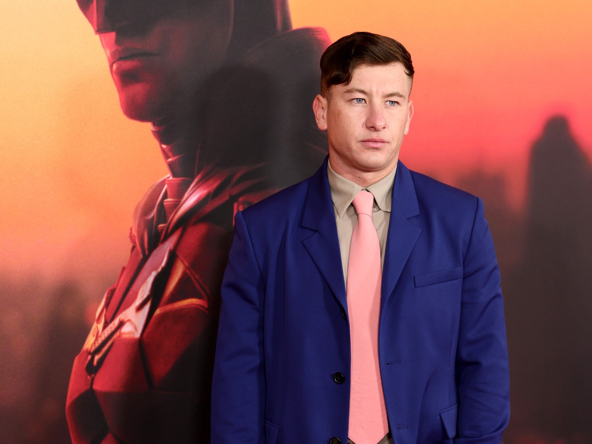 Barry Keoghan at 'The Batman' premiere. He's standing in front of a picture of Batman and wearing a blue suit and pink tie.