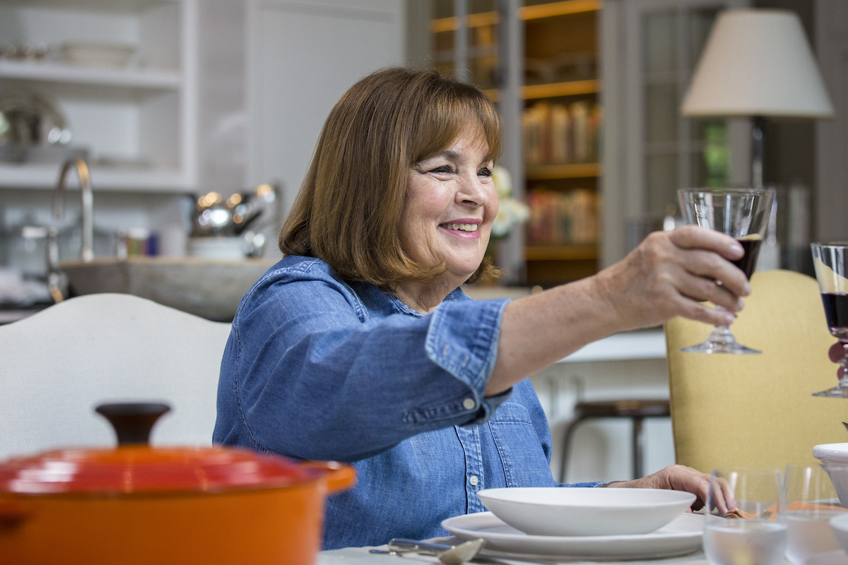 'Be My Guest With Ina Garten' host Ina Garten smiles holding up a glass while wearing a blue shirt