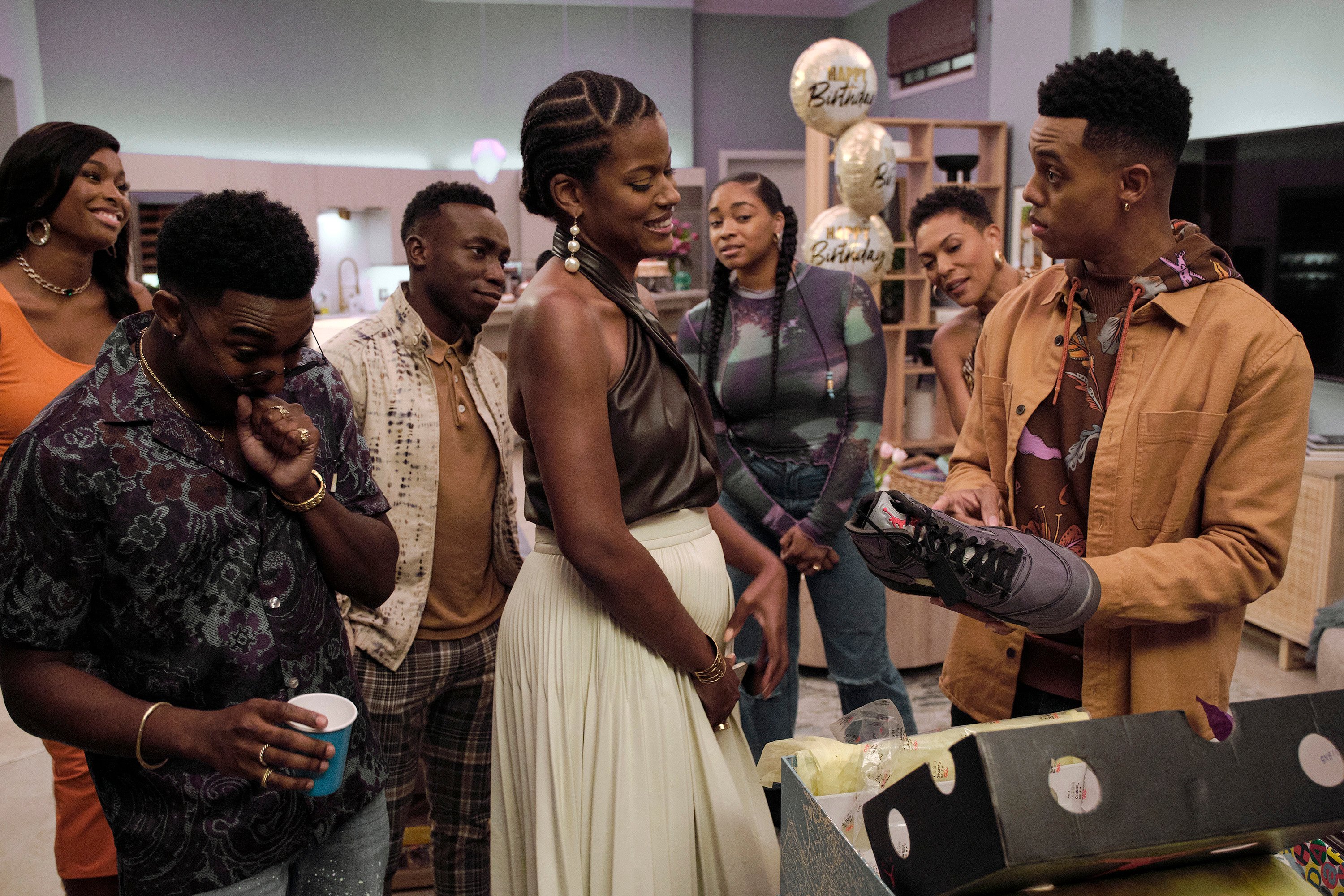 Coco Jones, Jordan L. Jones, Olly Sholotan, Cassandra Freeman, Simone Joy Jones, and April Parker Jones marveling at a pair of shoes Jabari Smith is holding