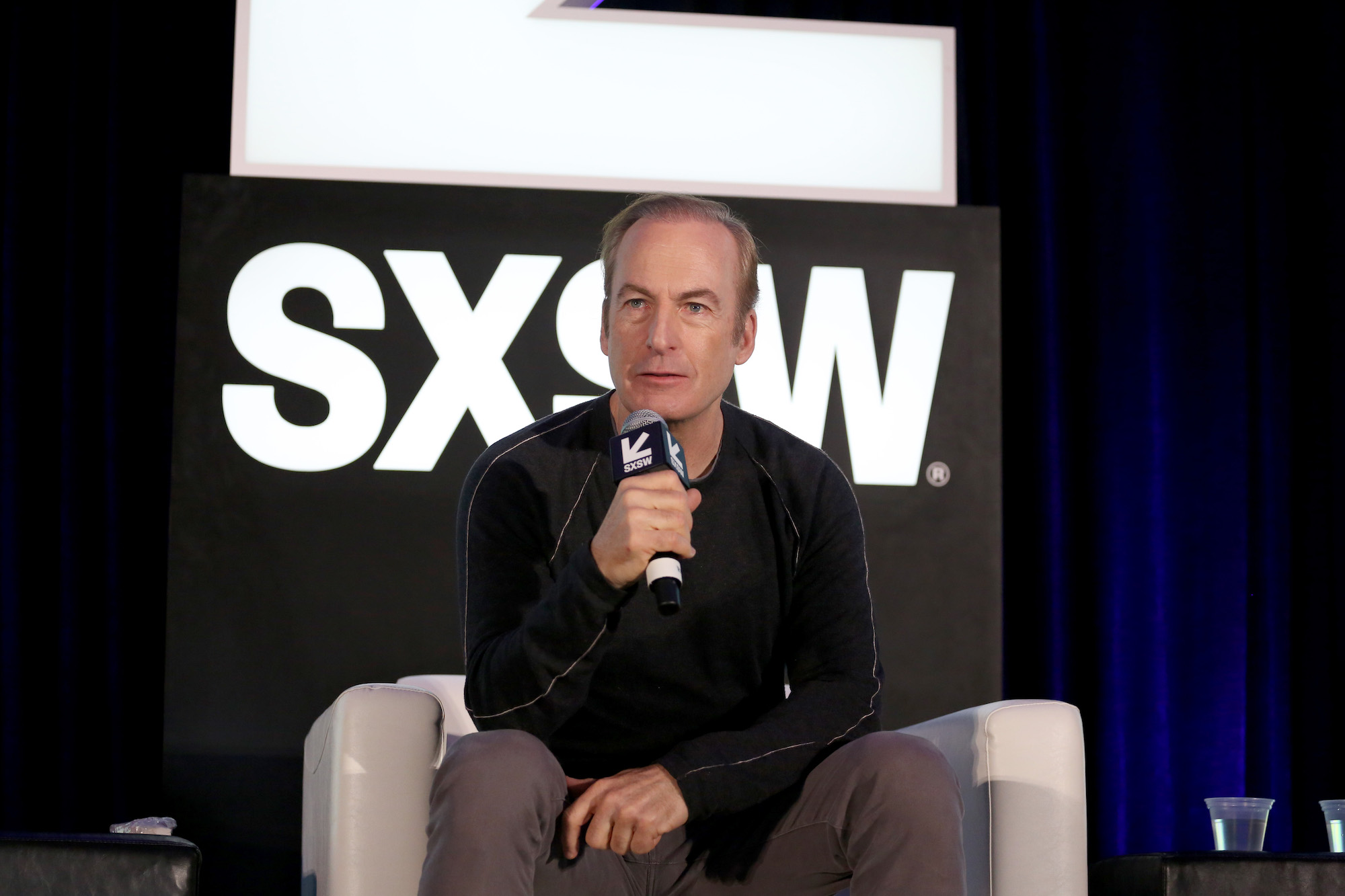'Better Call Saul' star Bob Odenkirk sits on a chair and speaks into a microphone at SXSW