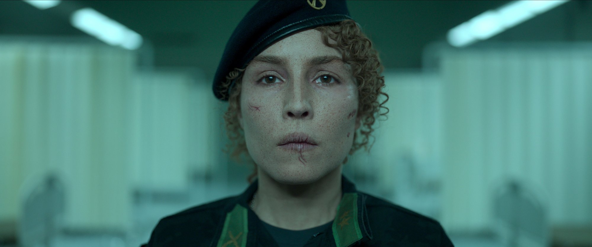 'Black Crab' Noomi Rapace as Caroline Edh looking straight ahead with cracked lips and a military hat