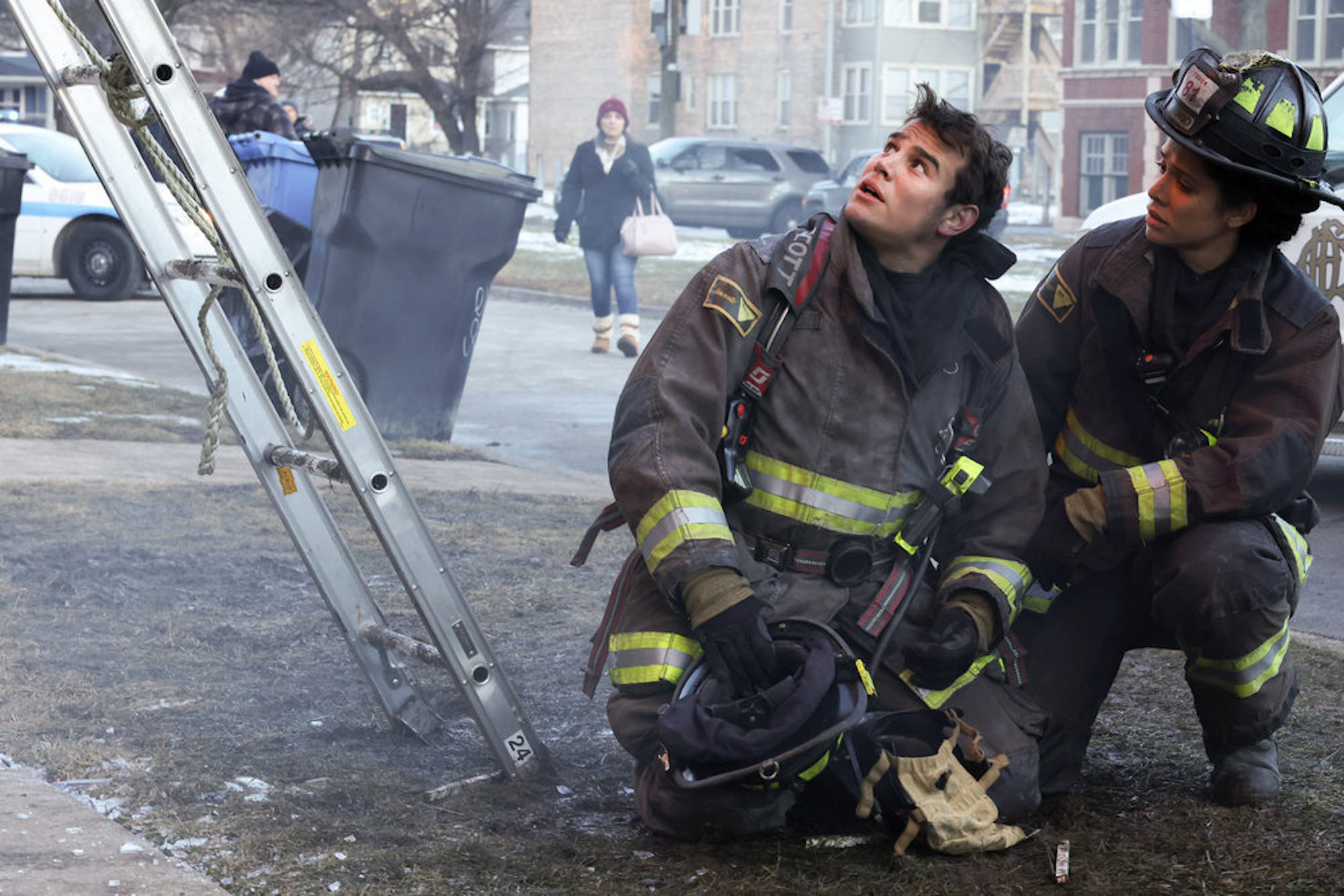 Alberto Rosende as Blake Gallo and Miranda Rae Mayo as Stella Kidd kneeling in rubble while in firefighting suits in 'Chicago Fire' Season 10