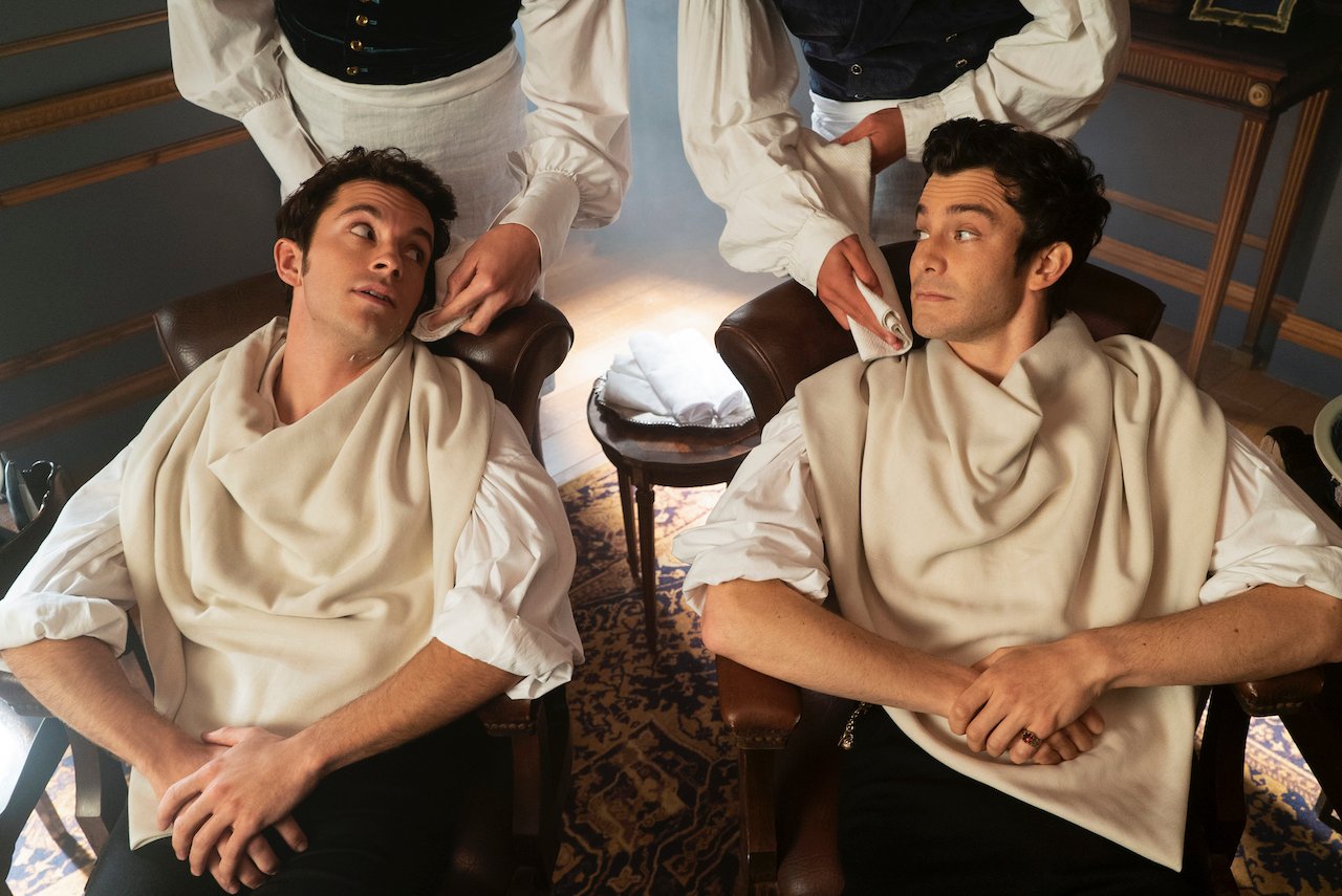 Jonathan Bailey as Anthony Bridgerton, Luke Thompson as Benedict Bridgerton look at each other as they sit getting their hair done in 'Bridgerton'.