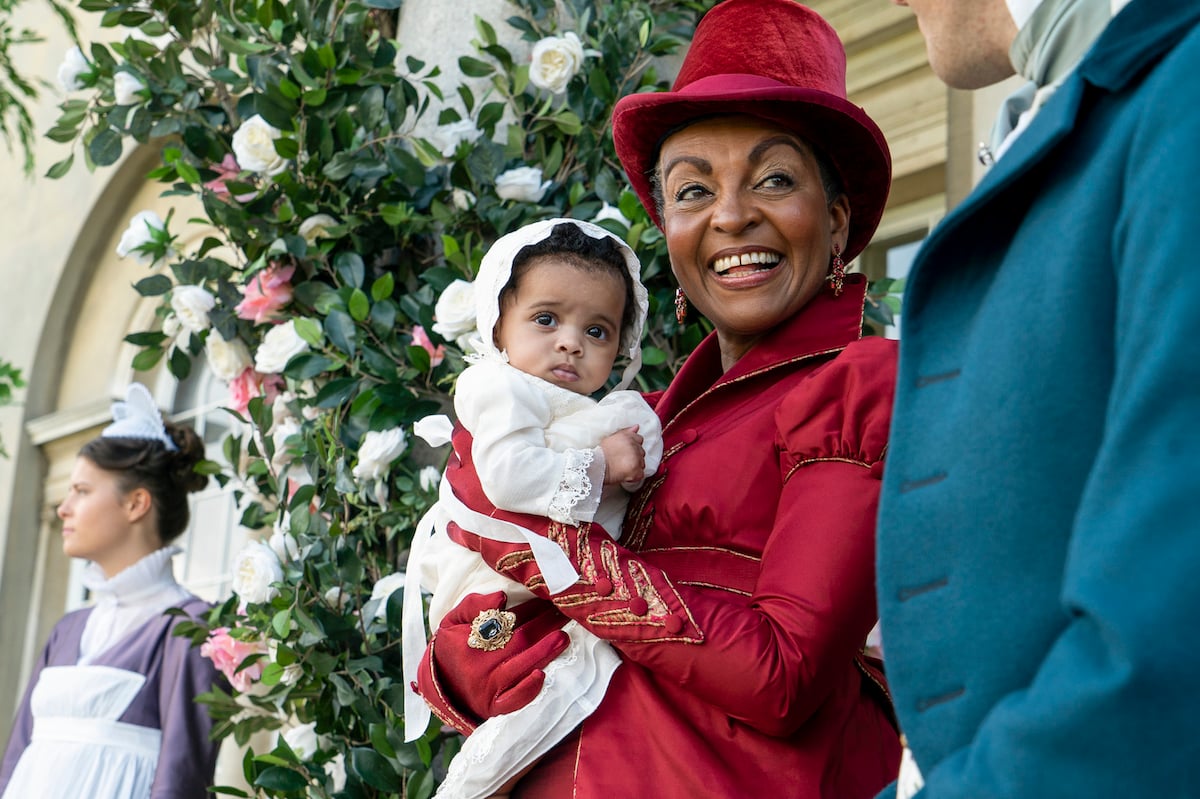 Lady Danbury, wearing a red hat and holding a baby, in 'Bridgerton' Season 2