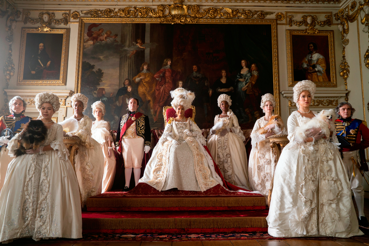 Hugh Sachs as Brimsley and Golda Rosheuvel as Queen Charlotte in Bridgerton Season 2. The Queen sits on her throne wearing a white gown.